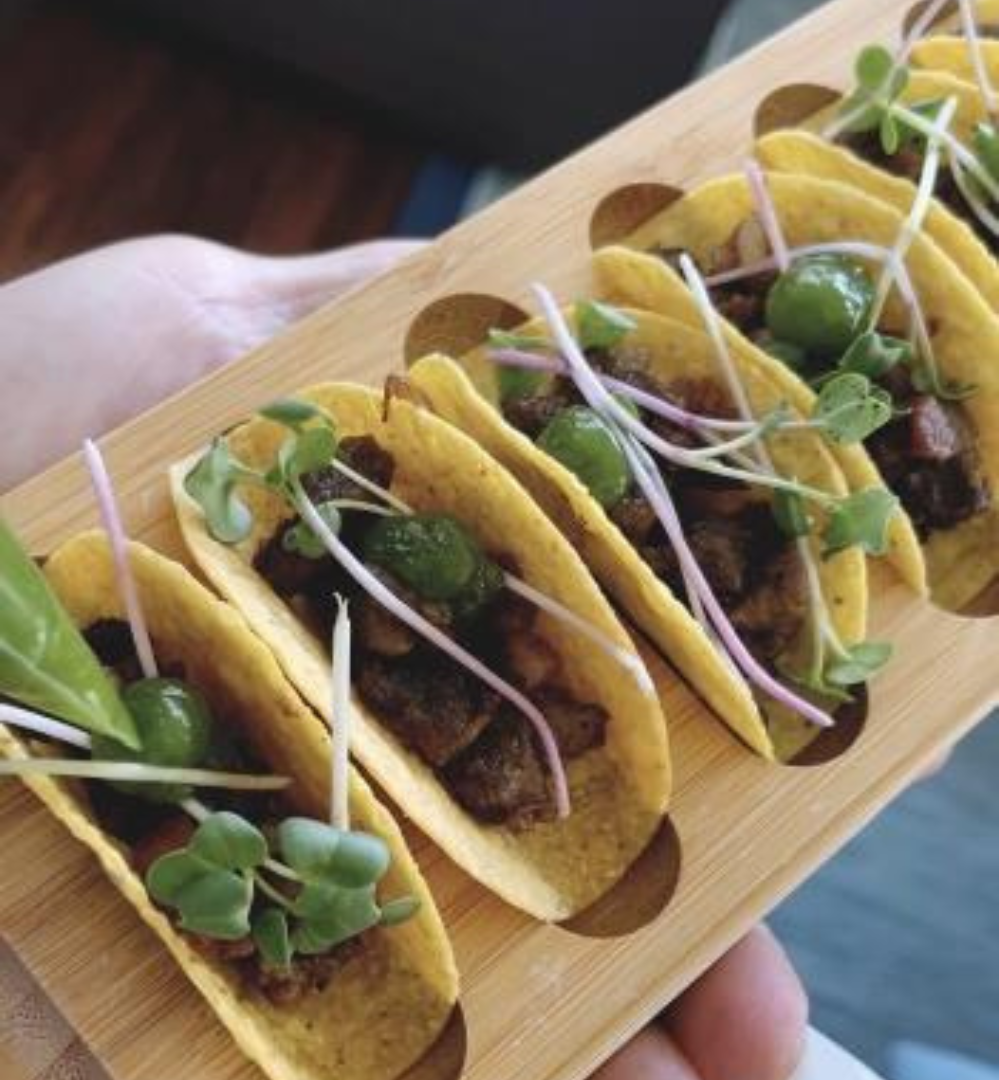 A person holding some tacos on a wooden board