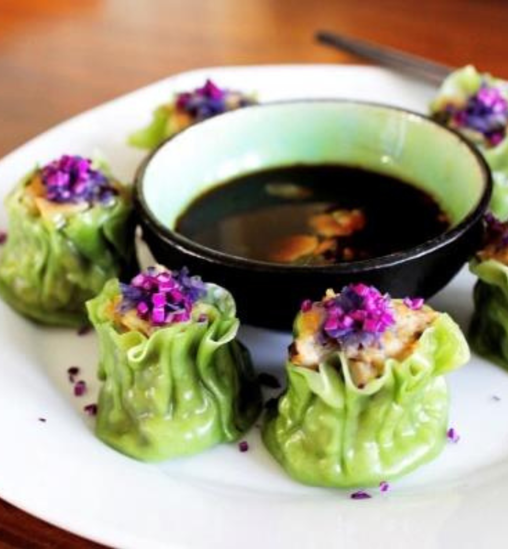 A plate of food with sauce and some purple flowers